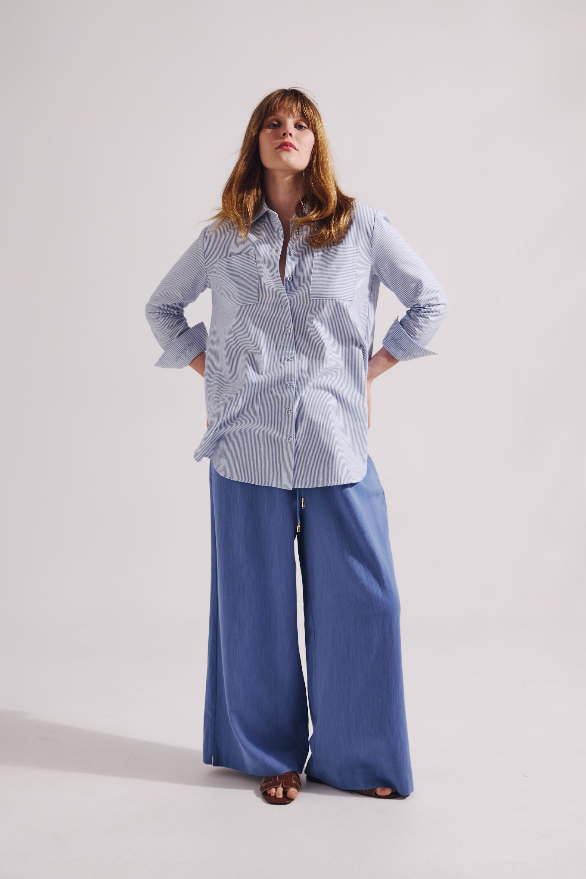 Woman wearing a light blue shirt and wide-leg pants on a white background