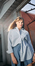 Woman wearing a light blue shirt and shorts standing in front of a brick building.