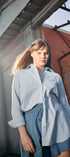 Woman wearing a light blue shirt and shorts standing in front of a brick building.
