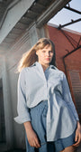 Woman wearing a light blue shirt and shorts standing in front of a brick building.