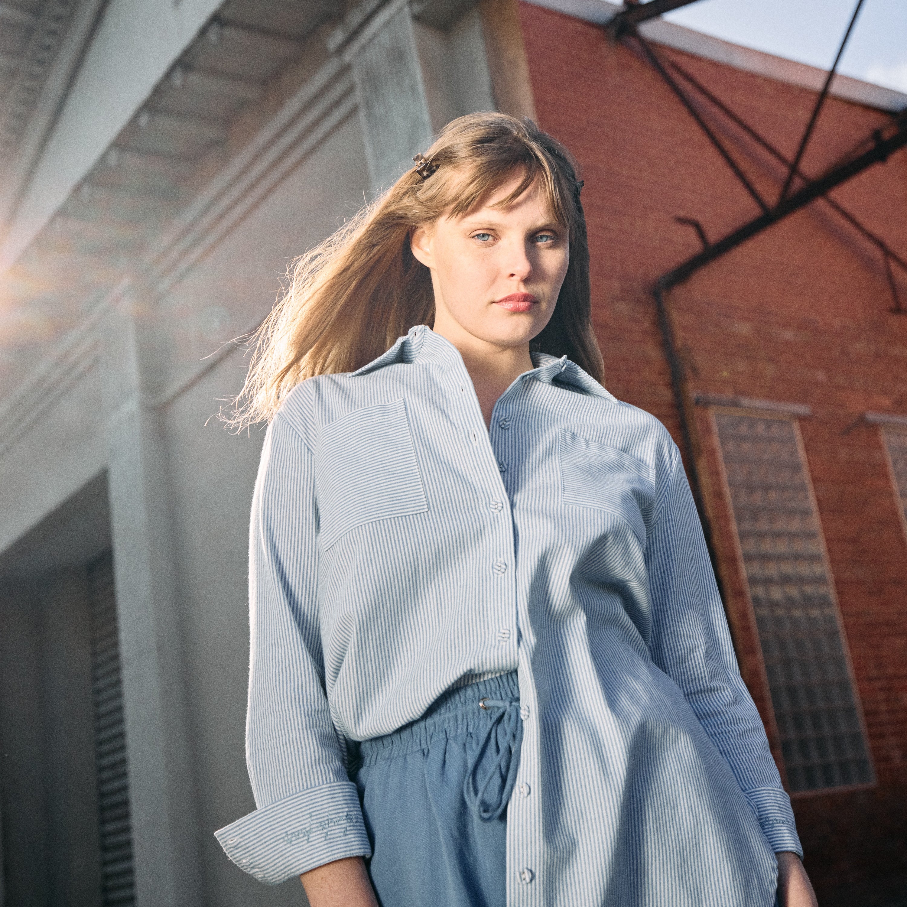 Woman wearing a light blue shirt and shorts standing in front of a brick building.