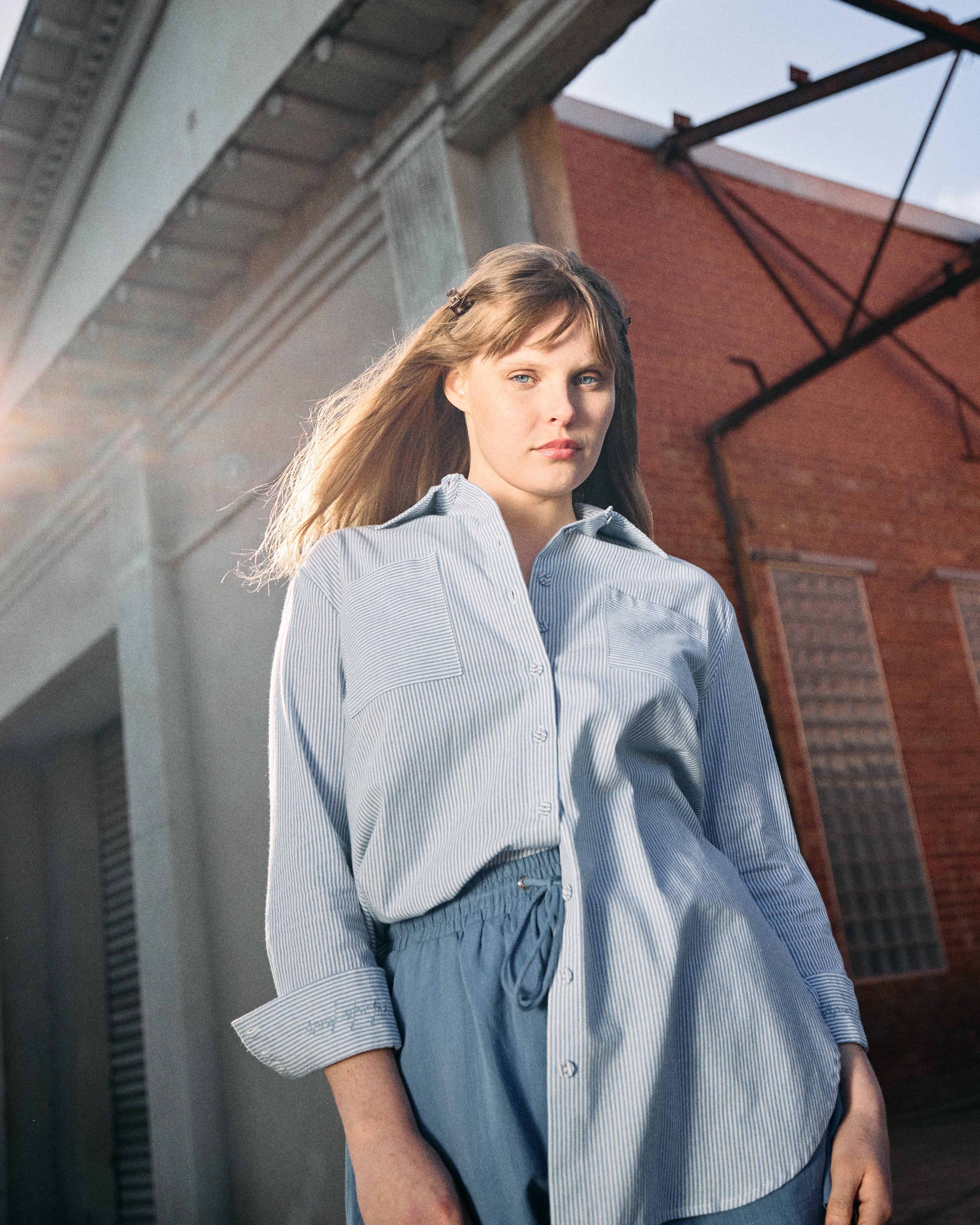 Woman wearing a light blue shirt and shorts standing in front of a brick building.