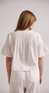 Person wearing a white blouse and pants against a plain background