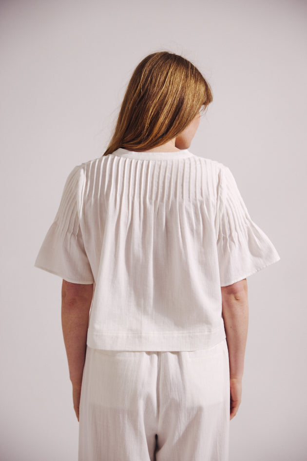 Person wearing a white blouse and pants against a plain background