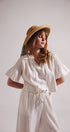 Woman wearing a white blouse and white pants with a straw hat on a plain background