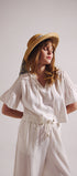 Woman wearing a white blouse and white pants with a straw hat on a plain background