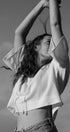 Person wearing a white blouse with arms raised against a clear sky