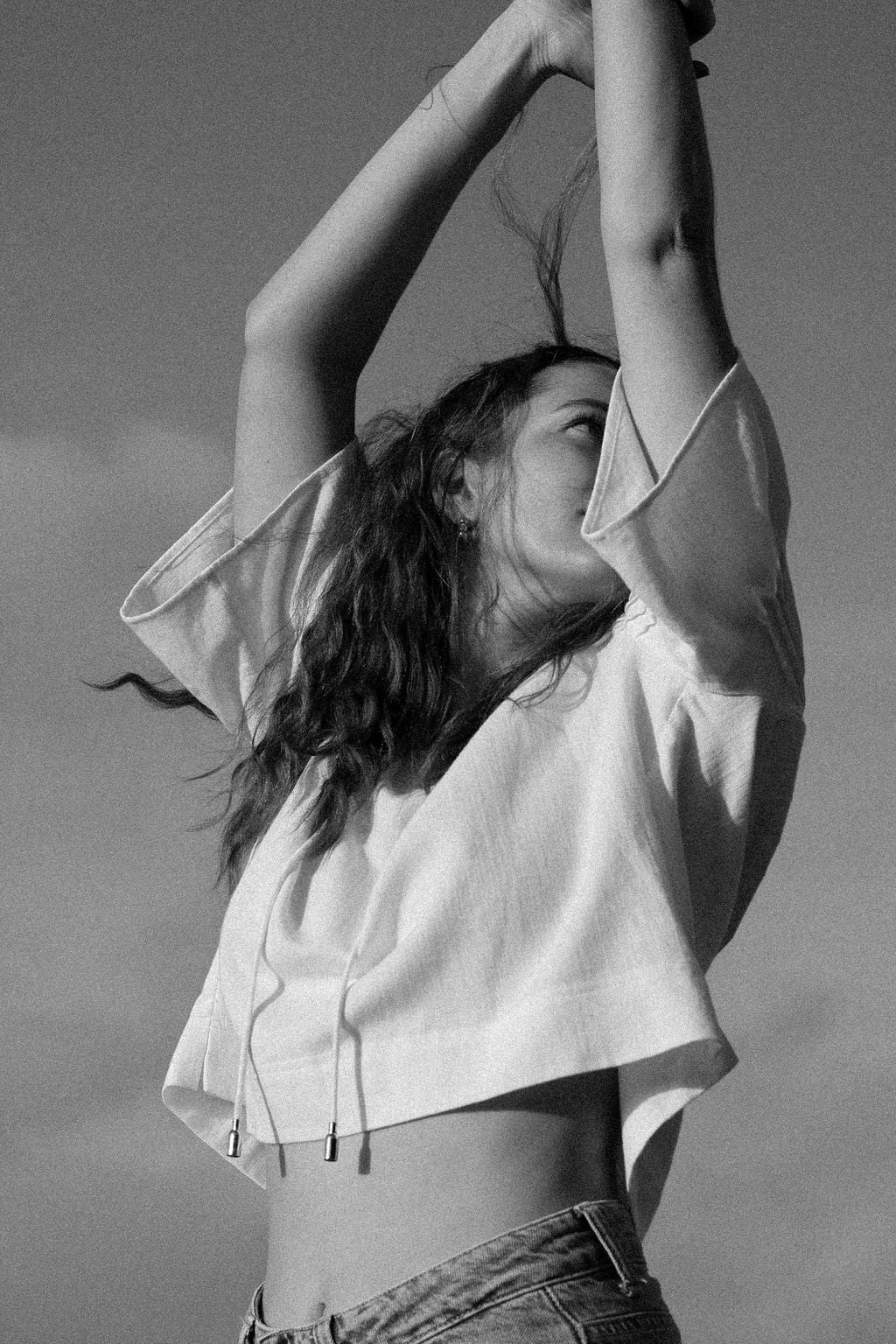 Person wearing a white blouse with arms raised against a clear sky