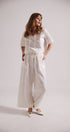 Woman wearing a white outfit with wide-leg pants on a plain background