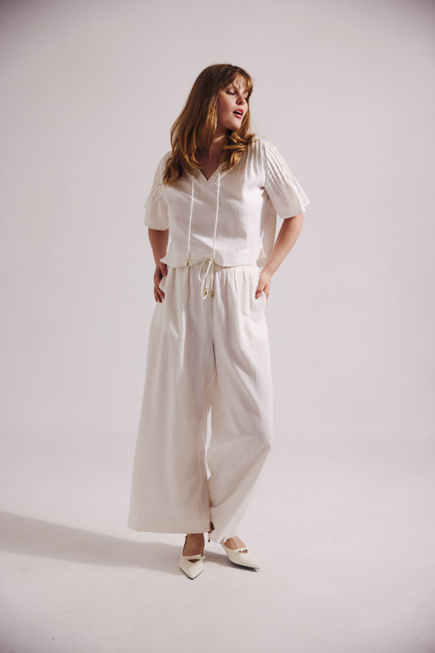 Woman wearing a white outfit with wide-leg pants on a plain background
