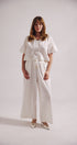 Woman wearing a white outfit with wide-leg pants on a plain background
