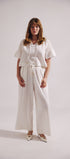 Woman wearing a white outfit with wide-leg pants on a plain background