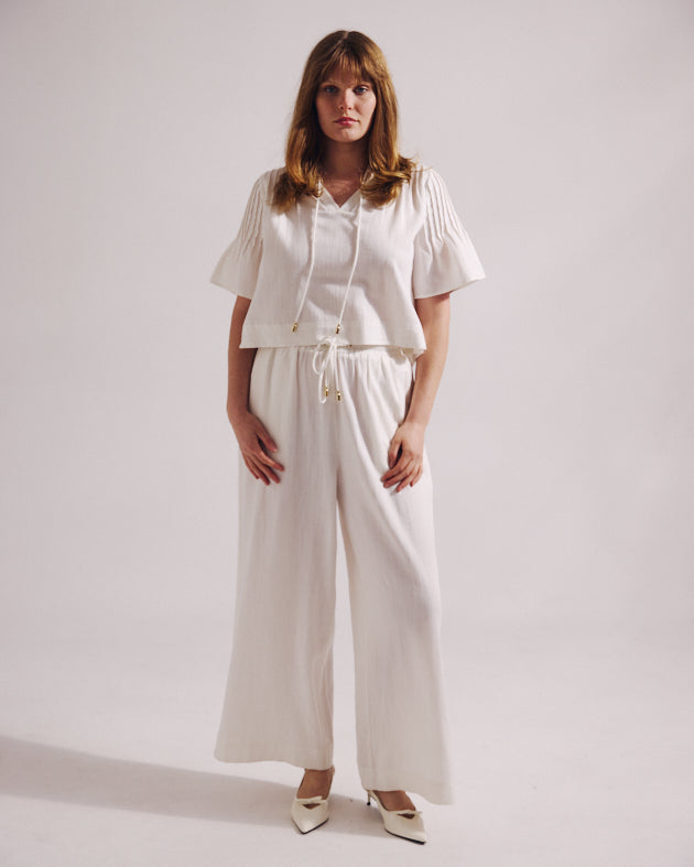 Woman wearing a white outfit with wide-leg pants on a plain background