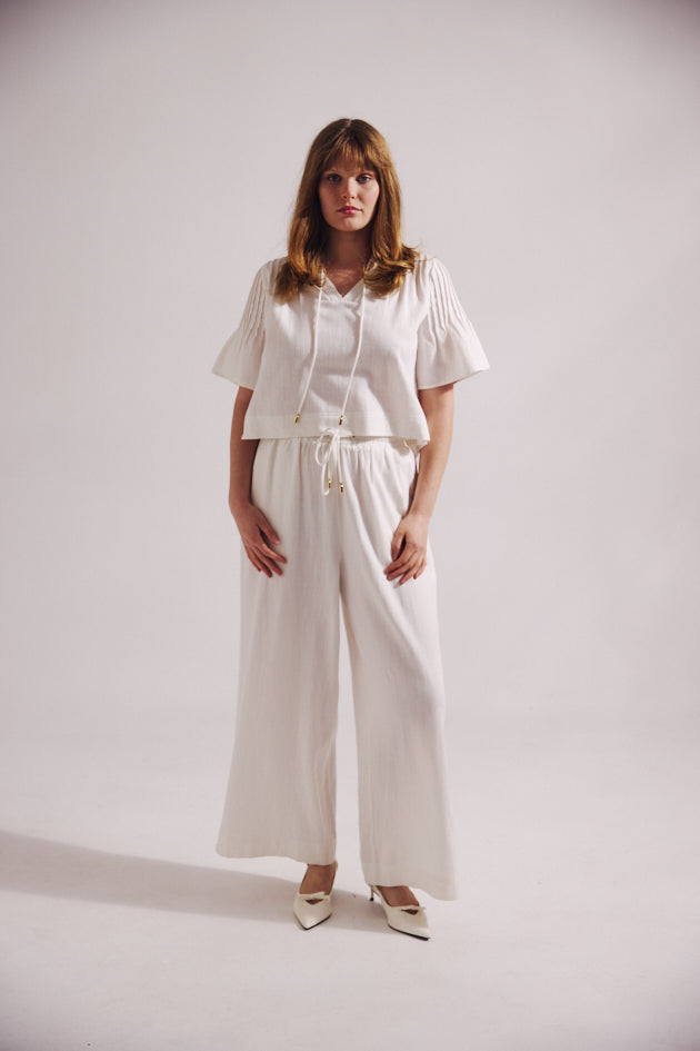 Woman wearing a white outfit with wide-leg pants on a plain background