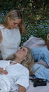 Two women sitting on a blanket in a garden with flowers and a basket.