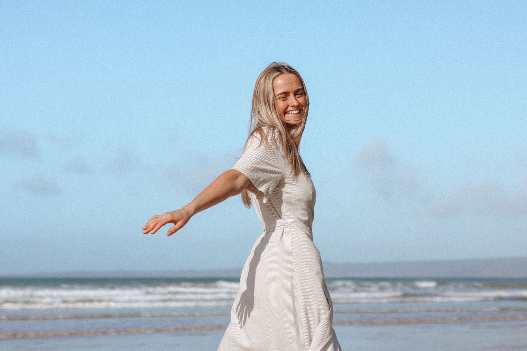 Woman in a white dress standing on a beach with a clear blue sky.
