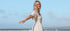 Woman in a white dress standing on a beach with a clear blue sky.