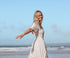 Woman in a white dress standing on a beach with a clear blue sky.