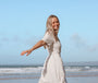 Woman in a white dress standing on a beach with a clear blue sky.