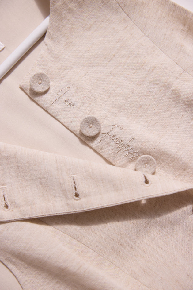 Close-up of a beige fabric with buttons and embroidered text on a light background