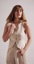 Woman wearing a beige sleeveless top and pants against a plain background