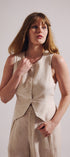 Woman wearing a beige sleeveless top and pants against a plain background