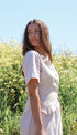 Woman in a white dress standing in a field with a clear blue sky.