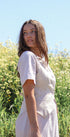 Woman in a white dress standing in a field with a clear blue sky.