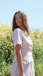 Woman in a white dress standing in a field with a clear blue sky.