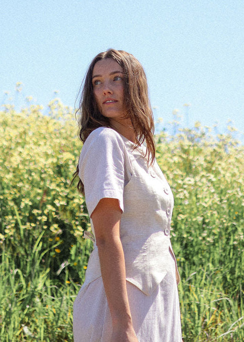 Woman in a white dress standing in a field with a clear blue sky.