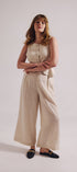 Woman wearing a beige sleeveless jumpsuit on a plain background