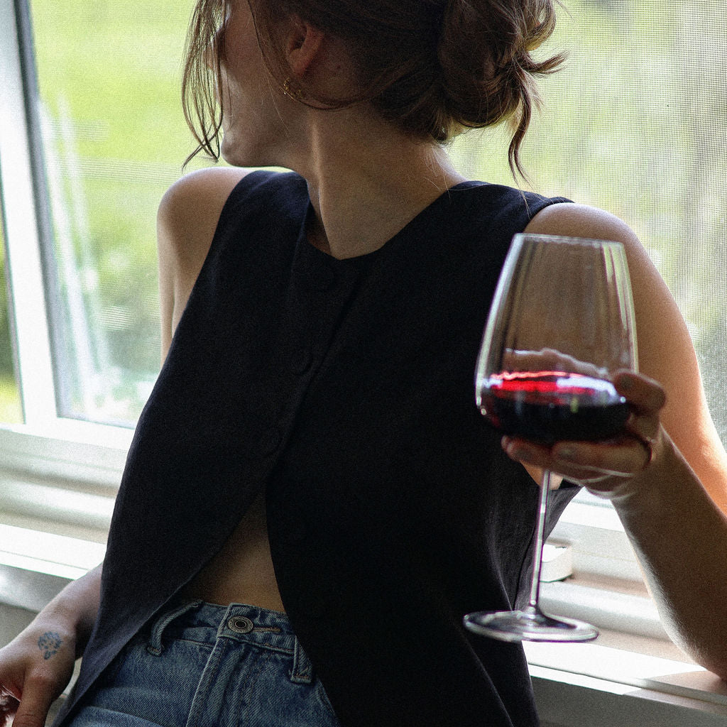 Person sitting by a window holding a glass of red wine