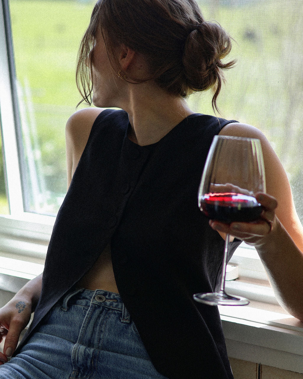 Person sitting by a window holding a glass of red wine