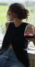 Person sitting by a window holding a glass of red wine