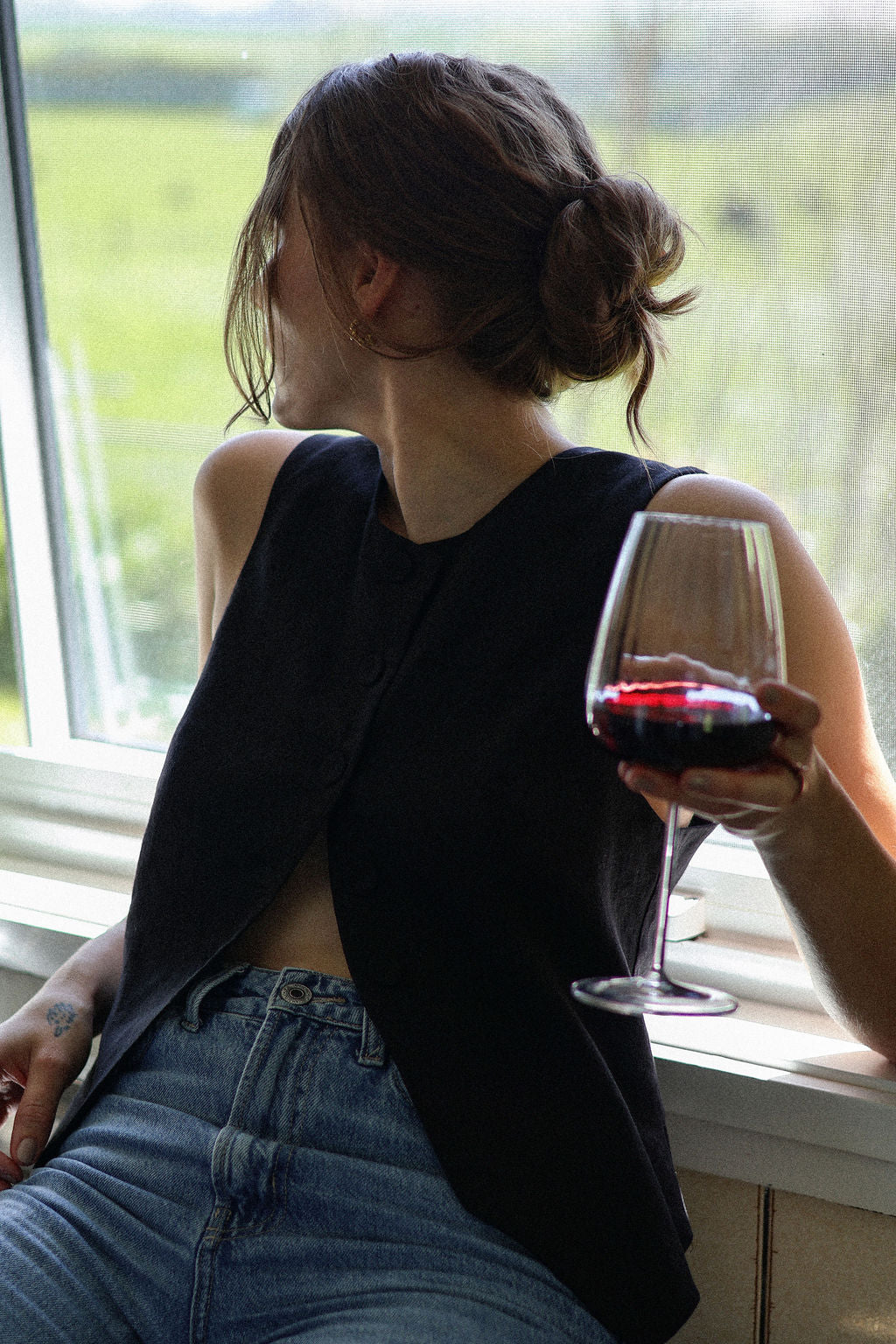 Person sitting by a window holding a glass of red wine