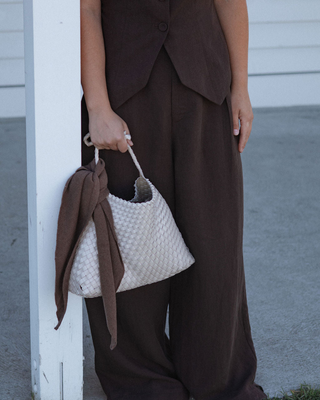 Person wearing a brown outfit holding a textured white handbag.