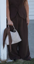 Person wearing a brown outfit holding a textured white handbag.
