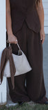 Person wearing a brown outfit holding a textured white handbag.