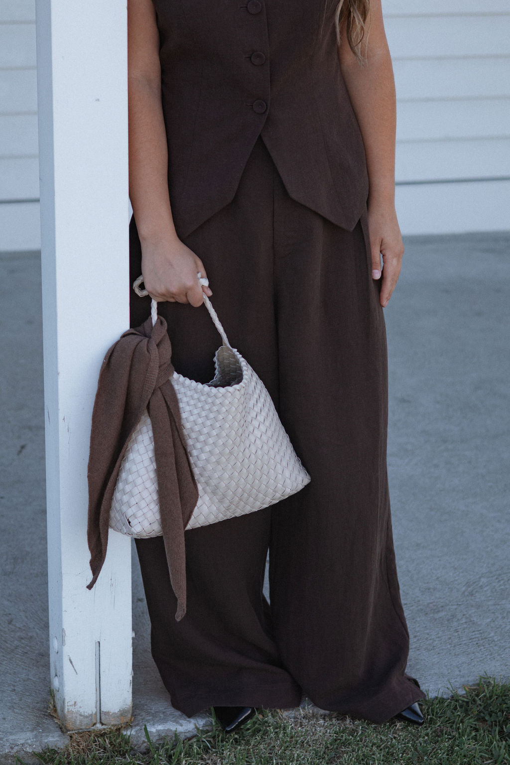 Person wearing a brown outfit holding a textured white handbag.