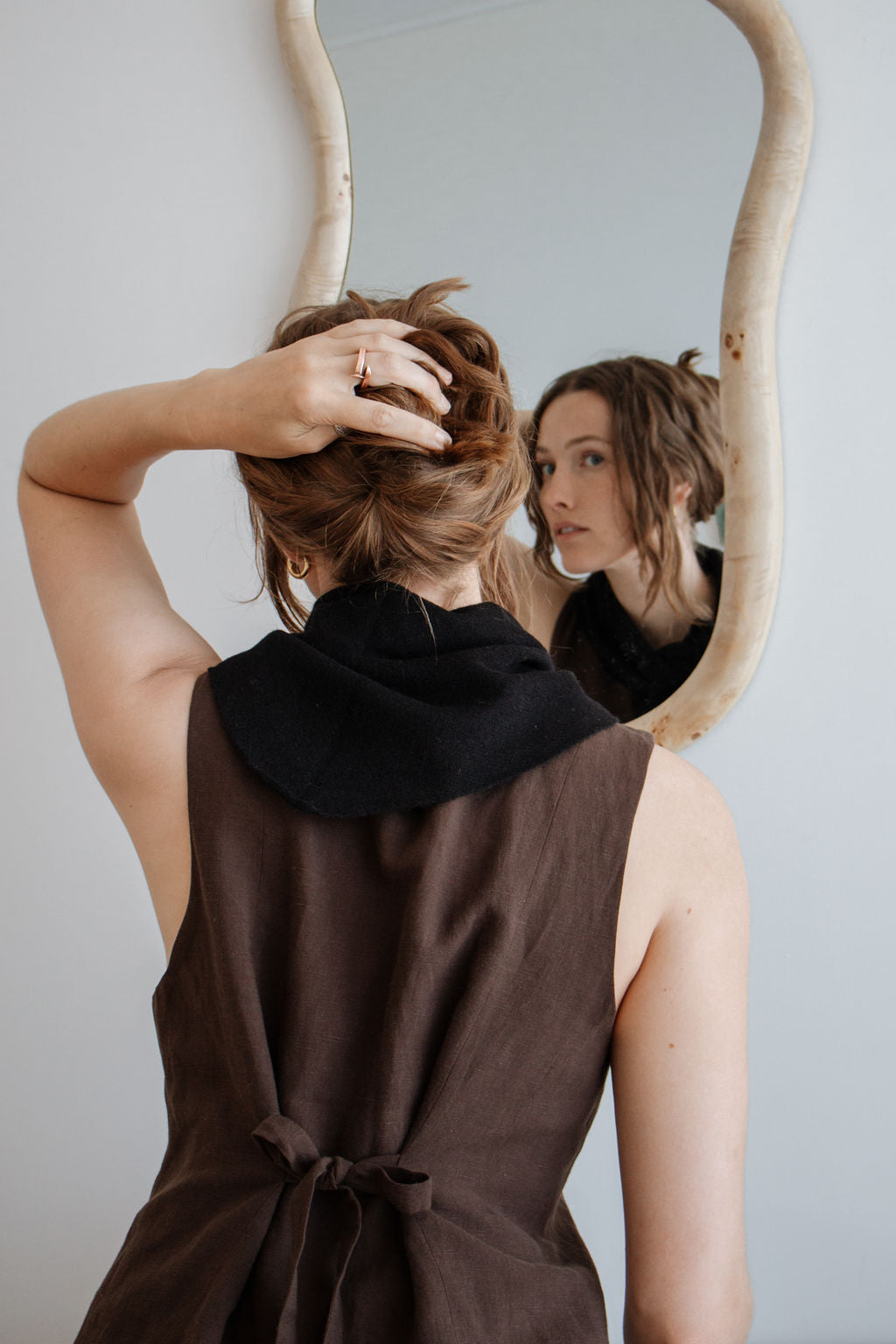Person adjusting hair in front of a mirror with a neutral background