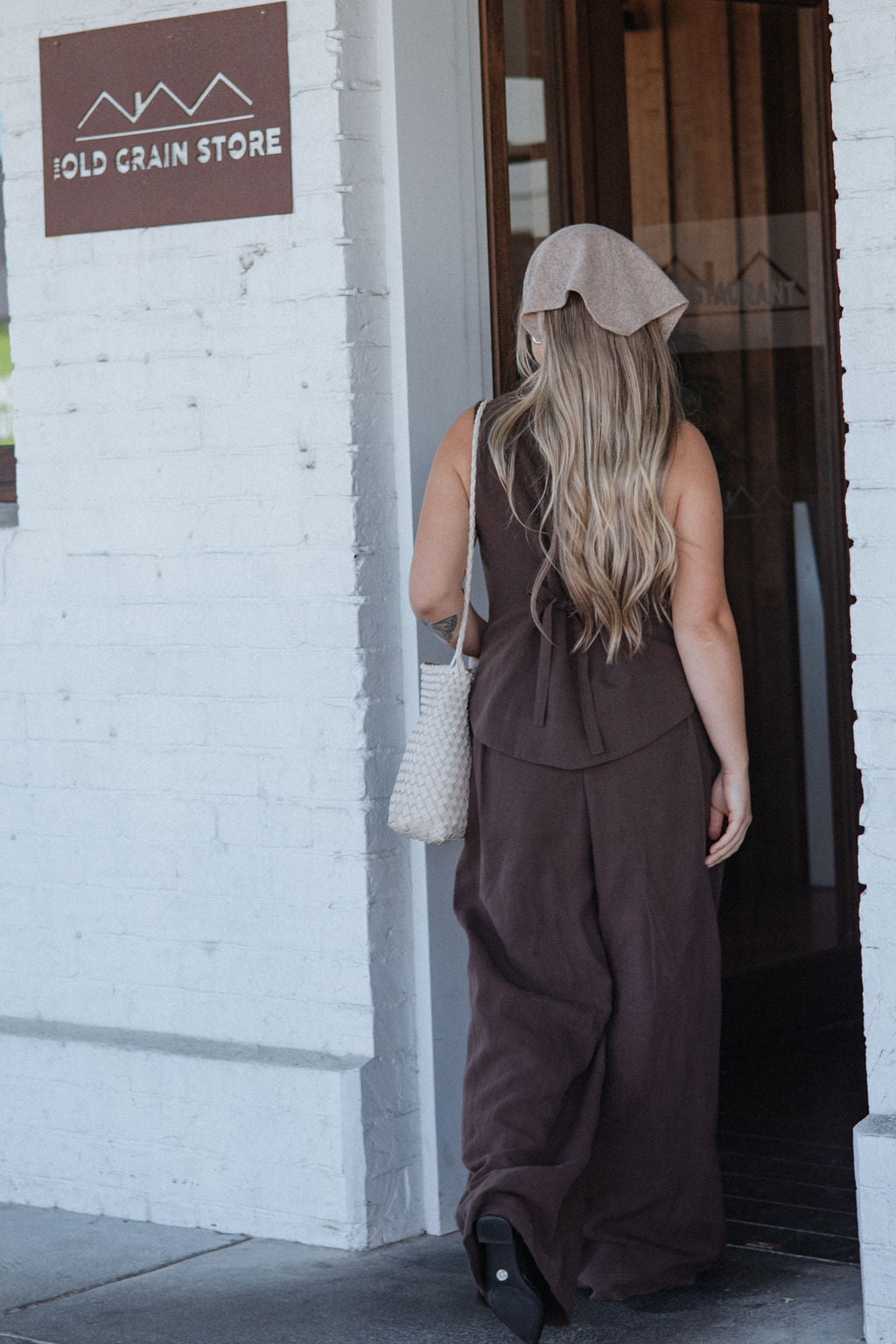 Person in a brown dress standing outside a building with a sign that reads 'Old Grain Store'.