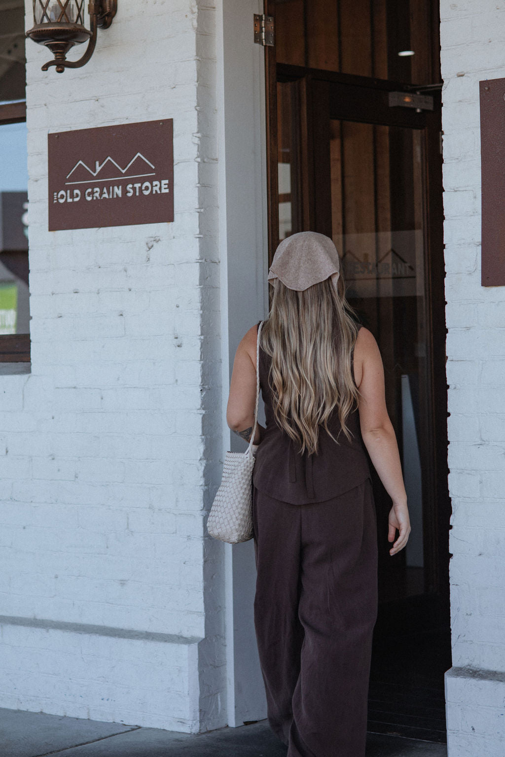 Woman entering a building with 'Gold Grain Store' sign on a white brick wall.