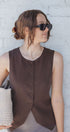Woman wearing a brown sleeveless top against a white brick wall