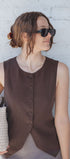 Woman wearing a brown sleeveless top against a white brick wall
