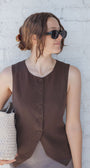 Woman wearing a brown sleeveless top against a white brick wall