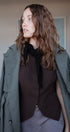 Woman wearing a green coat over a brown outfit indoors