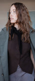 Woman wearing a green coat over a brown outfit indoors