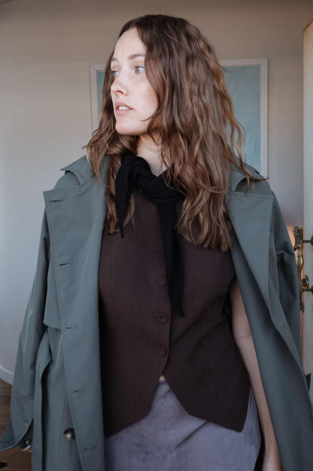 Woman wearing a green coat over a brown outfit indoors