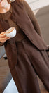Person wearing a brown outfit holding a cup, standing indoors.