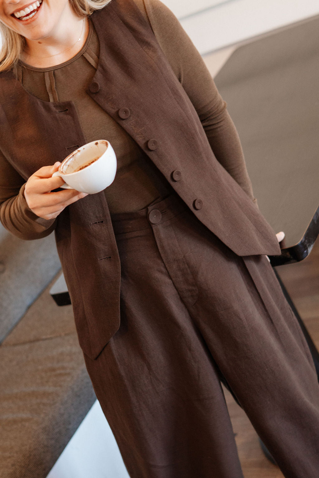 Person wearing a brown outfit holding a cup, standing indoors.